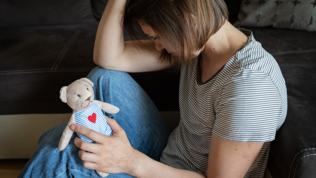Traurige Frau mit kleinem Kuscheltier Bären in der Hand